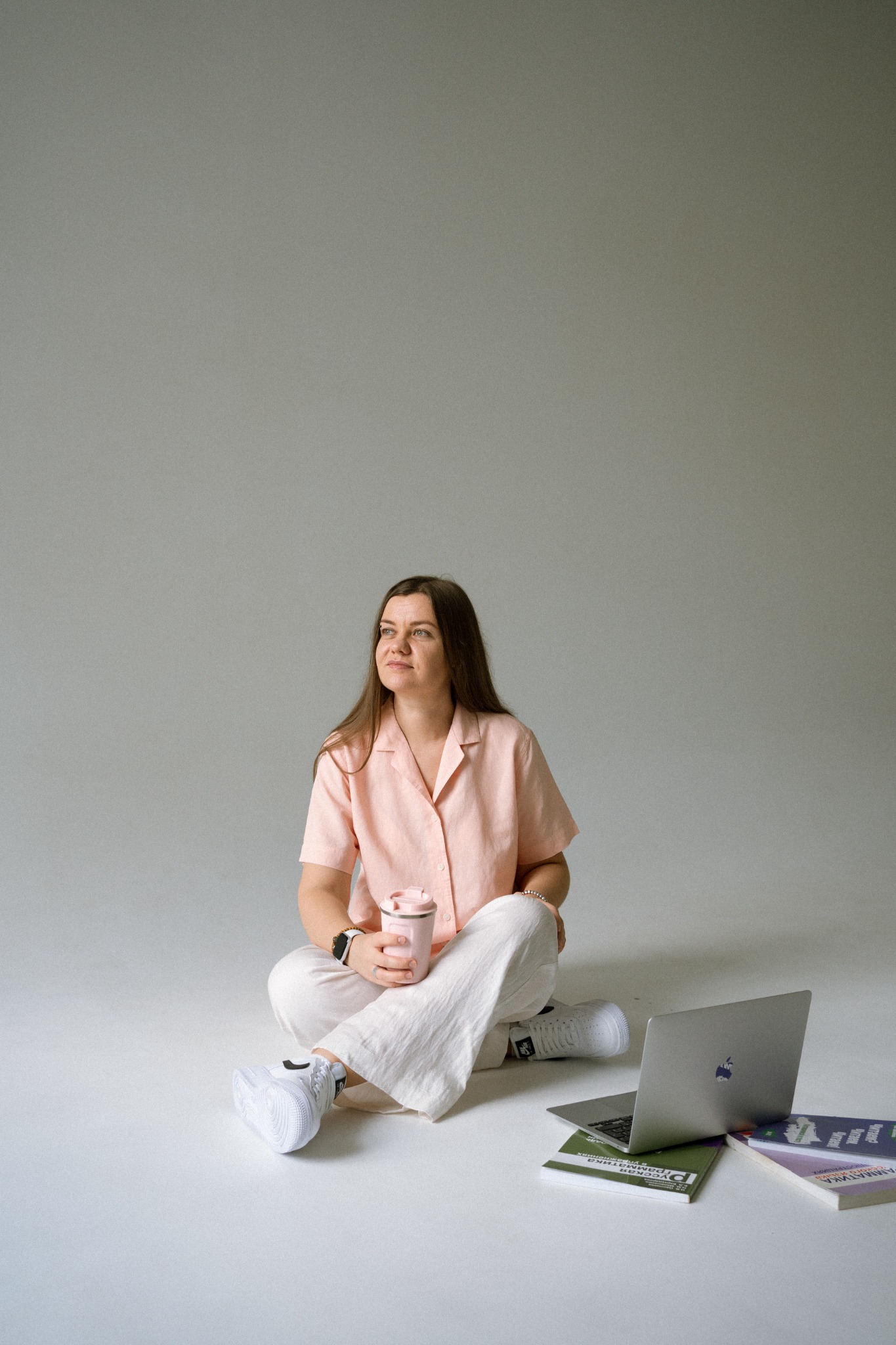 Anna sitting with her laptop, Russian books and a pink cup